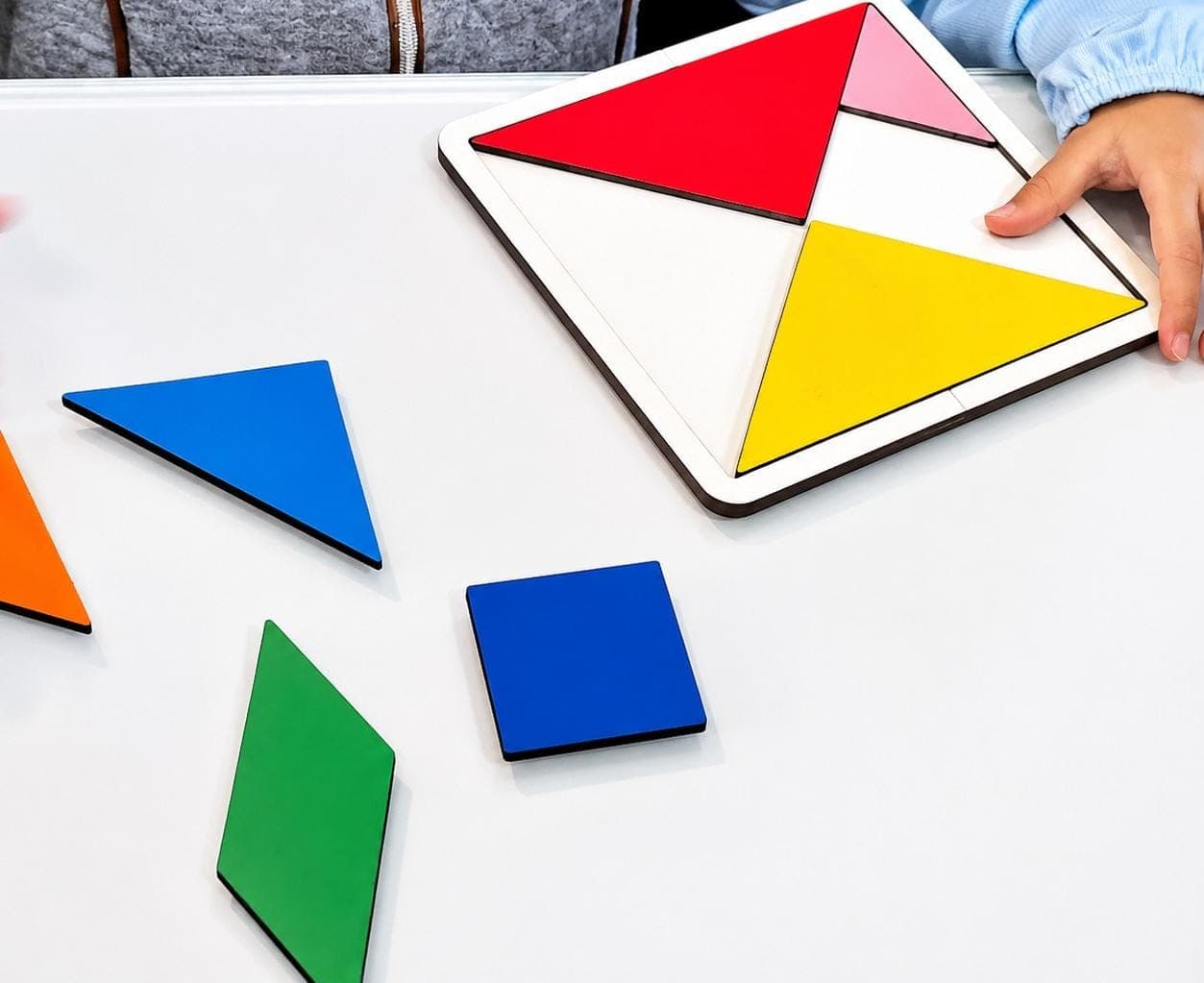 Criança montando o tangram na base de MDF, com as peças soltas sobre a mesa